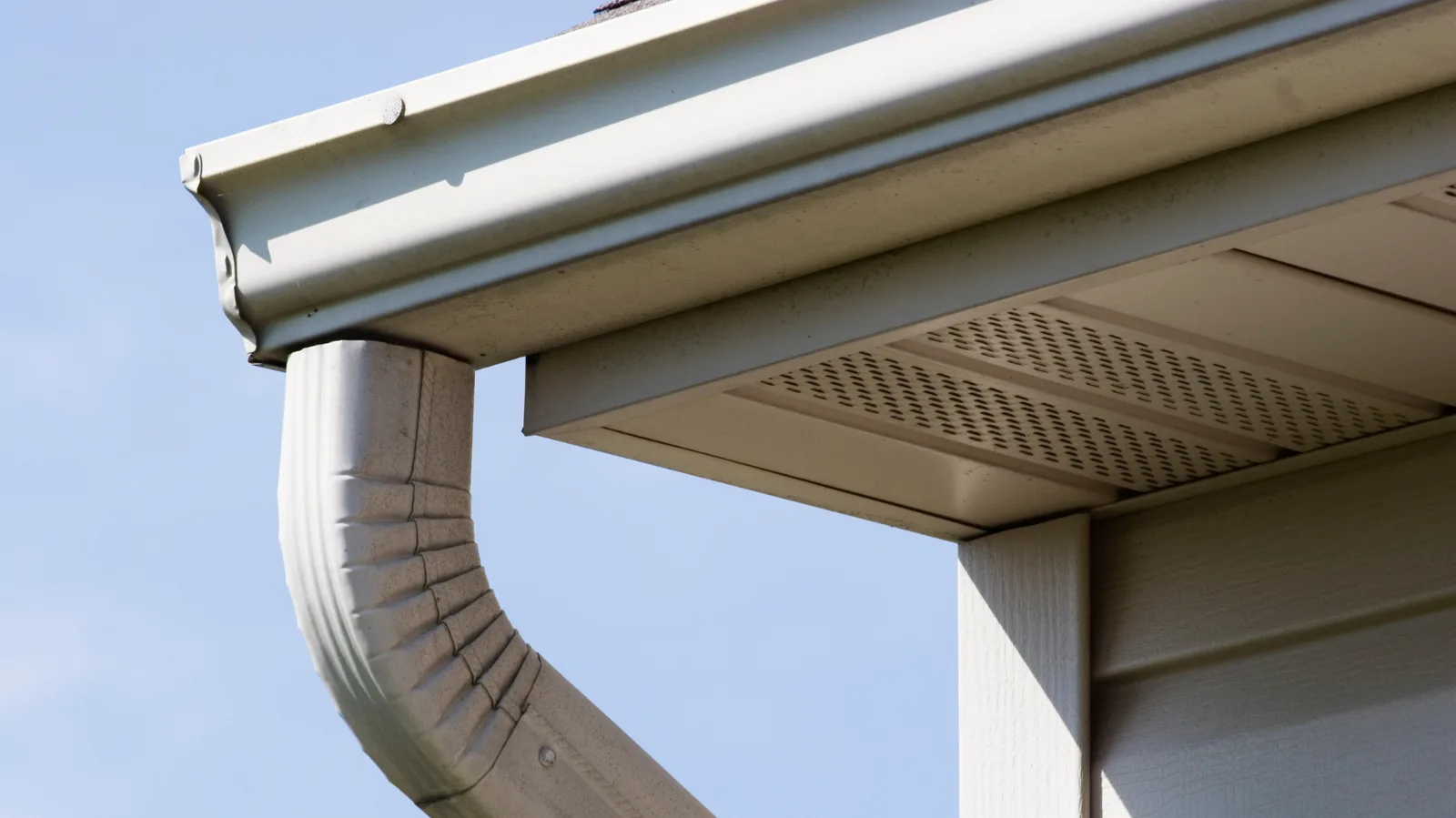 White gutter and downspout at a corner with vented soffit